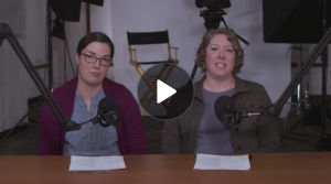 Screenshot with play button of two instructors seated at a table and speaking