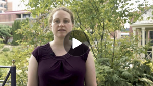 Screenshot with play button of an instructor standing outdoors with trees and a garden behind her.